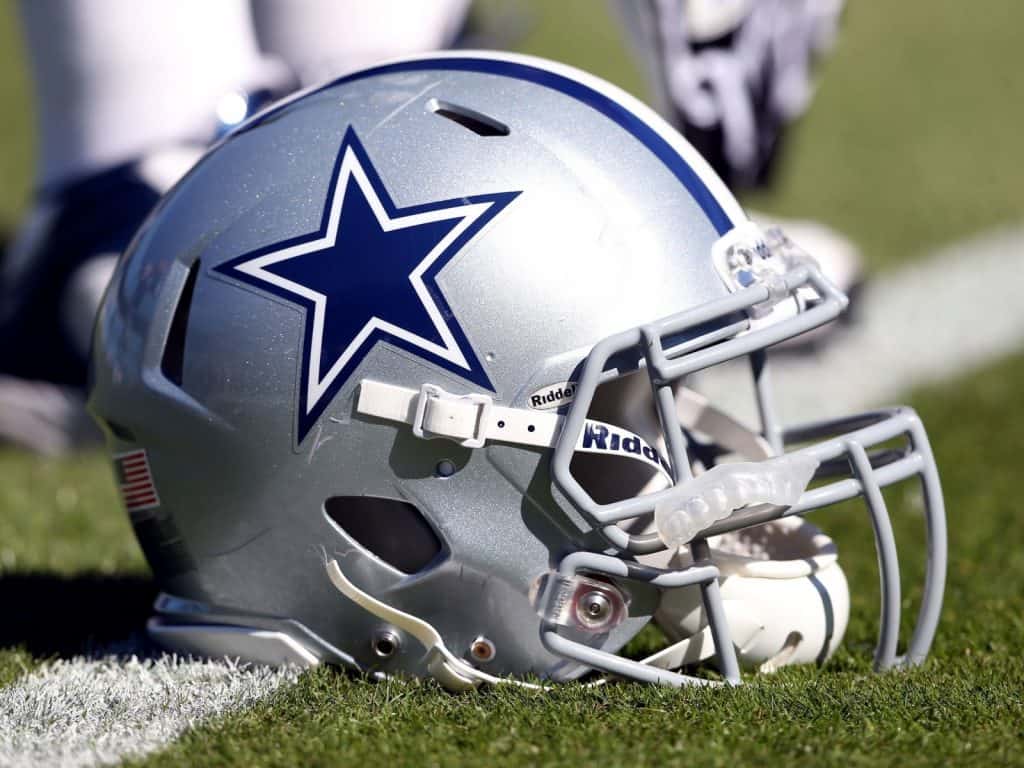 A Dallas Cowboys football helmet sits on the turf of a football field on a yard marker line.