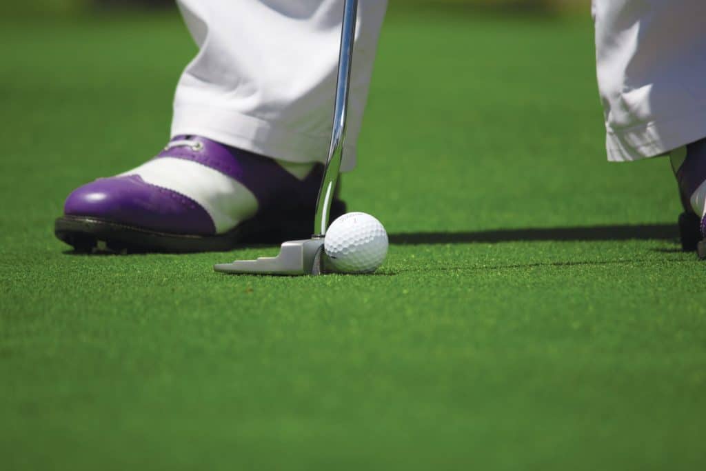 Golfer with purple and white shoes putting a golf ball on a green