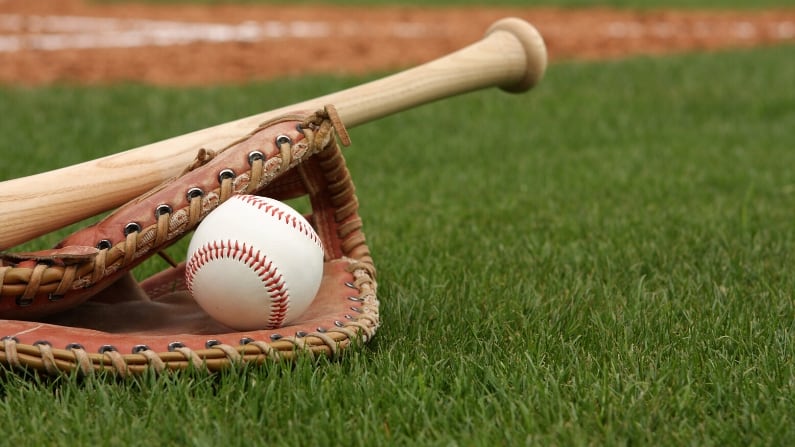 Bat, glove, and ball sitting on a baseball diamond.