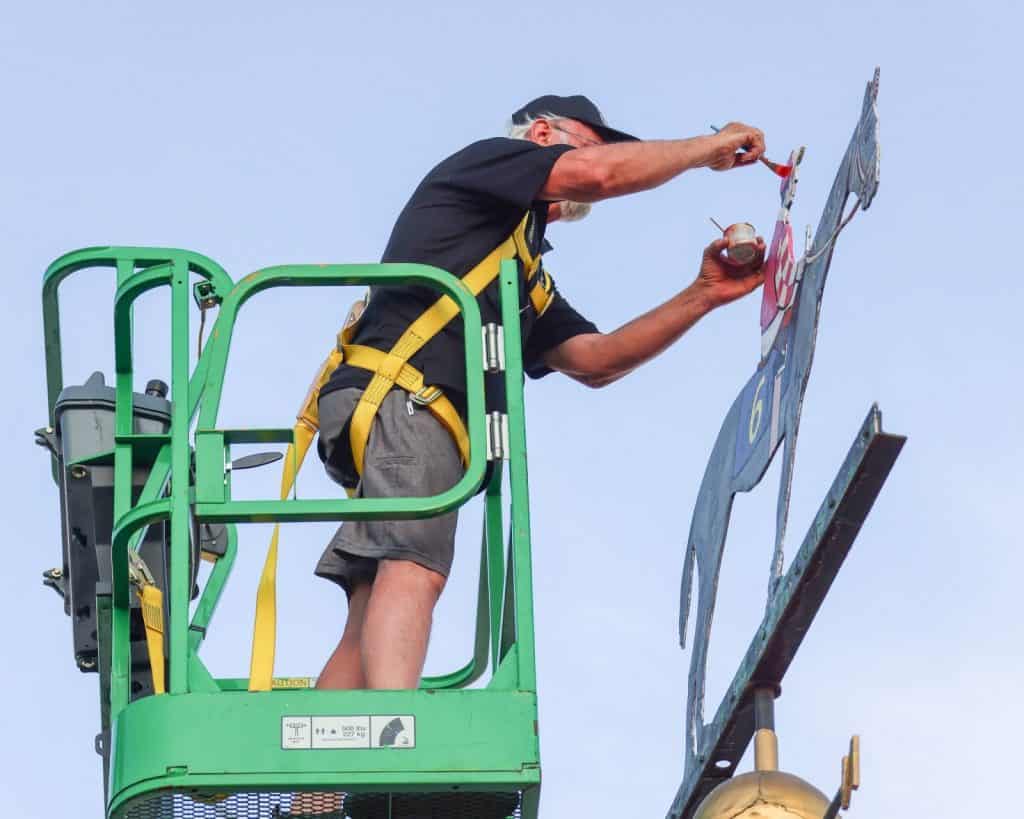 A man repaints the colors of the jockey's silks on the weathervane atop a replica of the Old Clubhouse cupola.