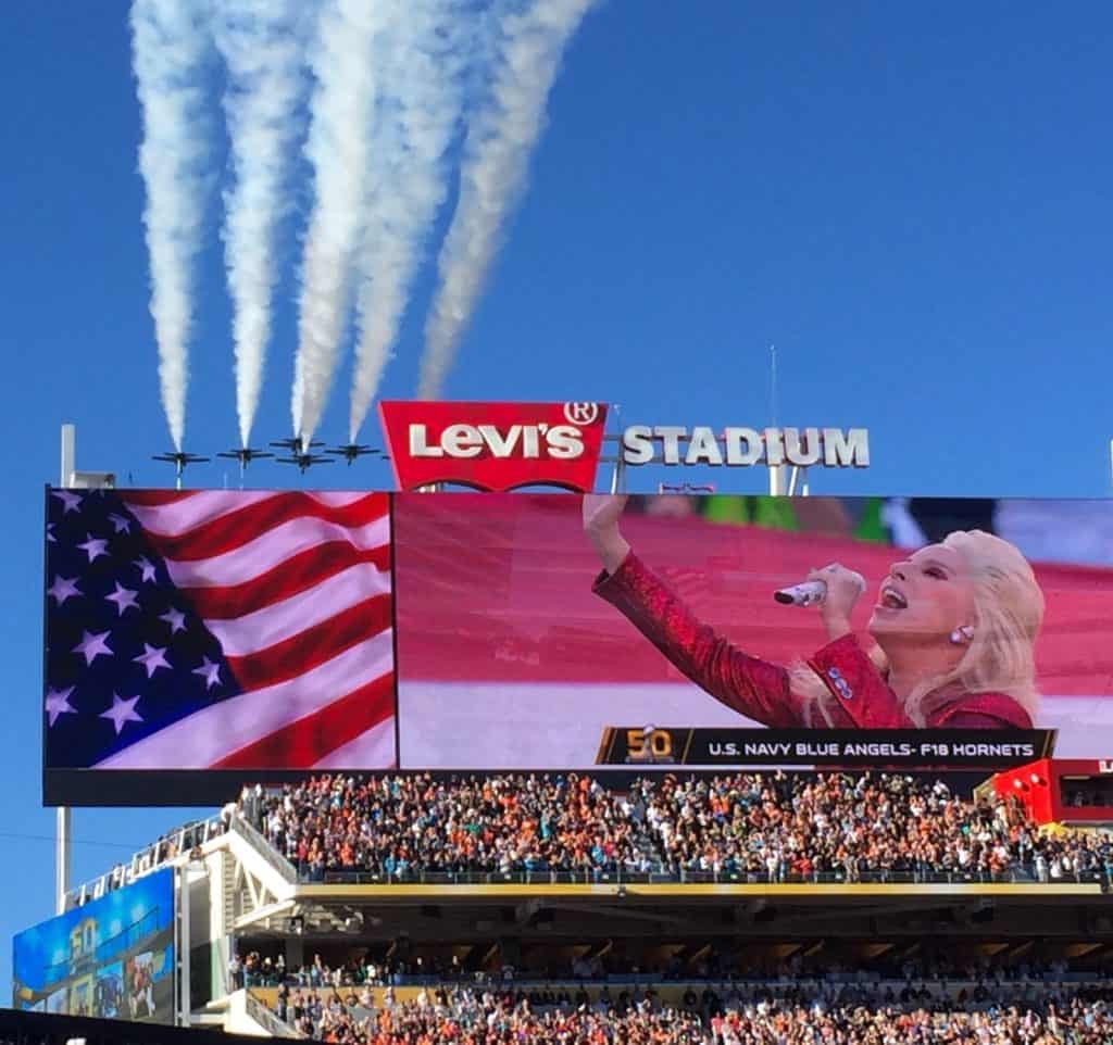 The scoreboard at Levi's Stadium showing a close-up of Lady Gaga singing the national anthem as U.S. Navy Blue Angels and F18 Hornets perform the traditional military flyover at Levi's Stadium before Super Bowl 50 - February 7, 2016